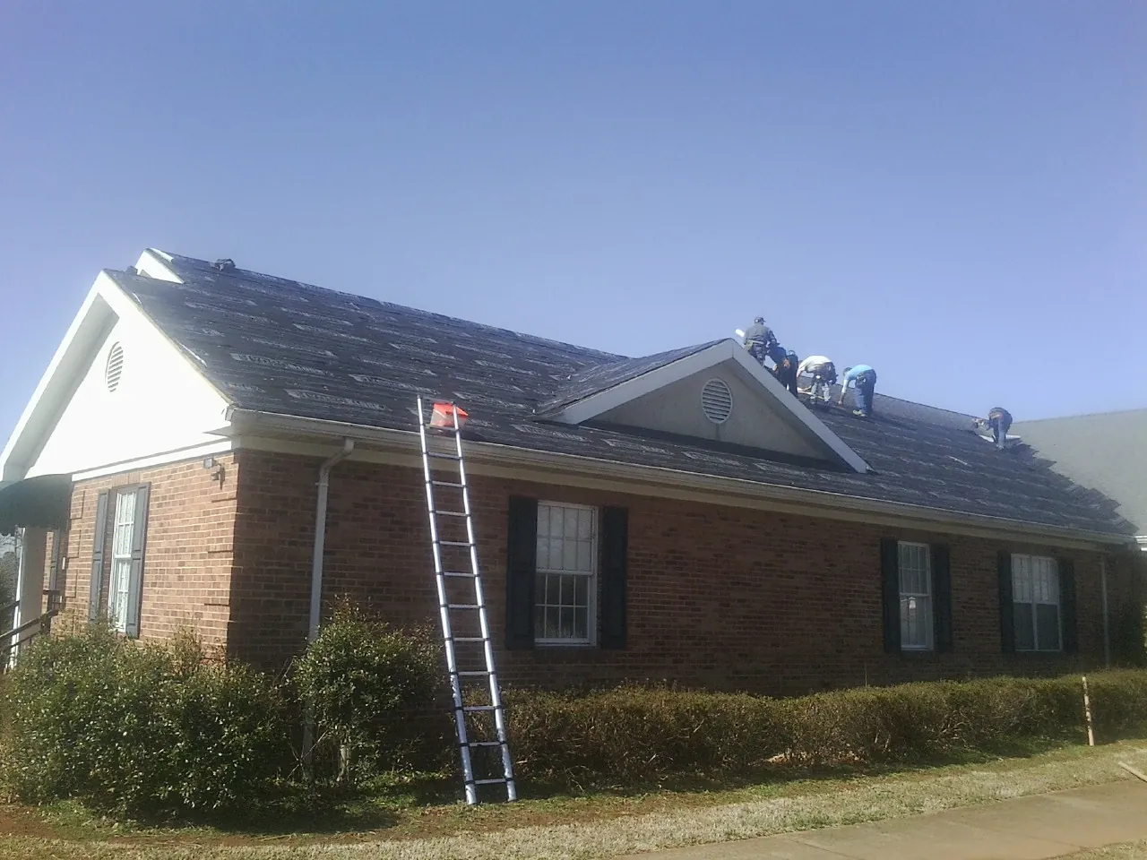 Crew tearing shingles off a brick ranch roof with a ladder set — Emergency Roof Repair work by our crew in Hinckley