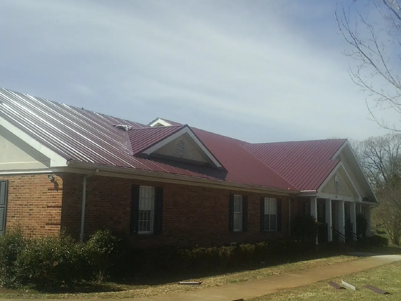 Red metal roof with gabled entries on a long brick building, from a Hail Damage Roof Repair job in Hinckley