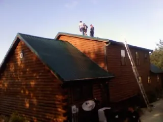 Crew on the ridge of a green metal roof on a two story log home in Hinckley