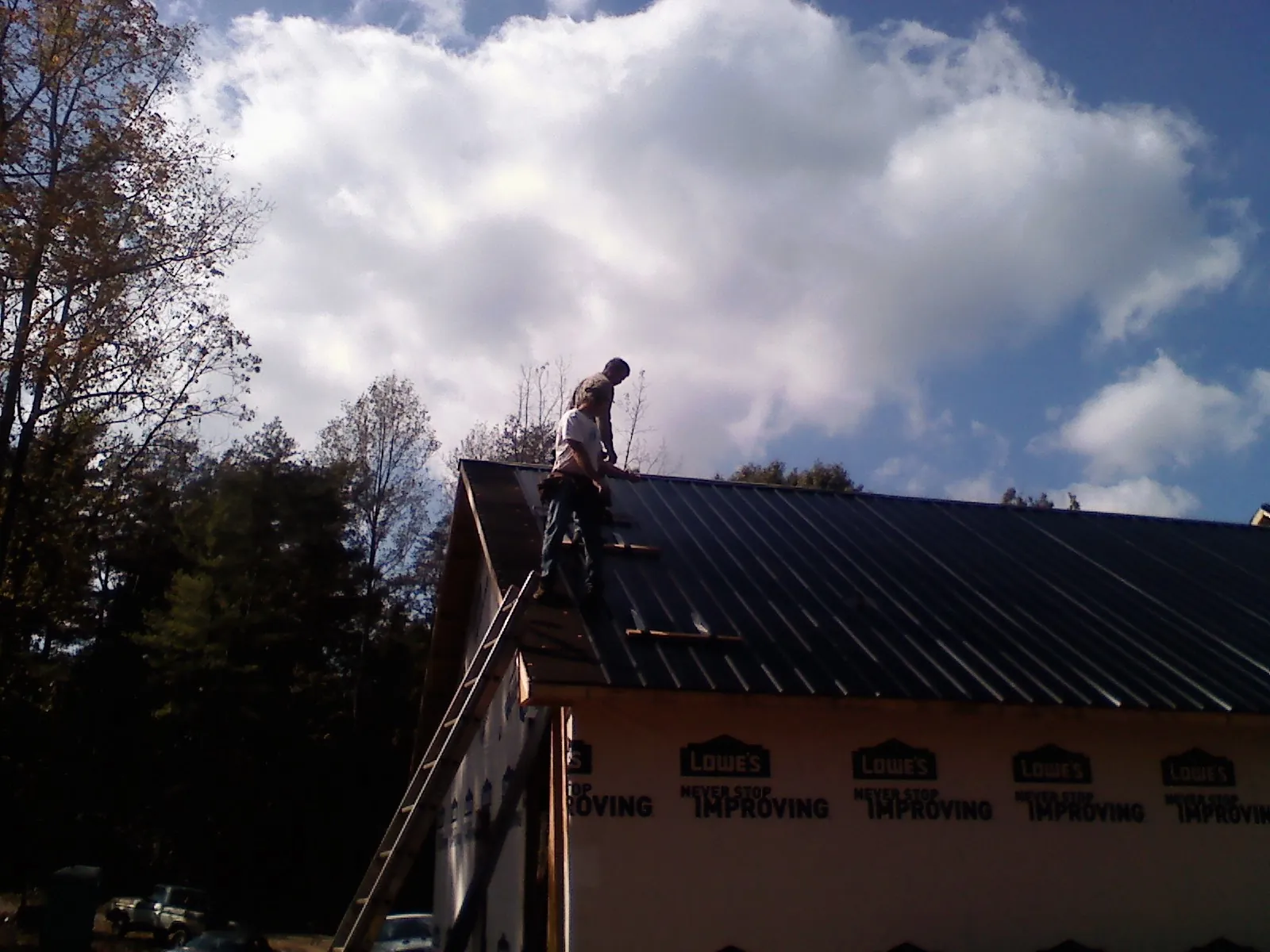 Roofer fastening dark metal panels high against a cloudy sky, from a Roof Inspection job in Hinckley
