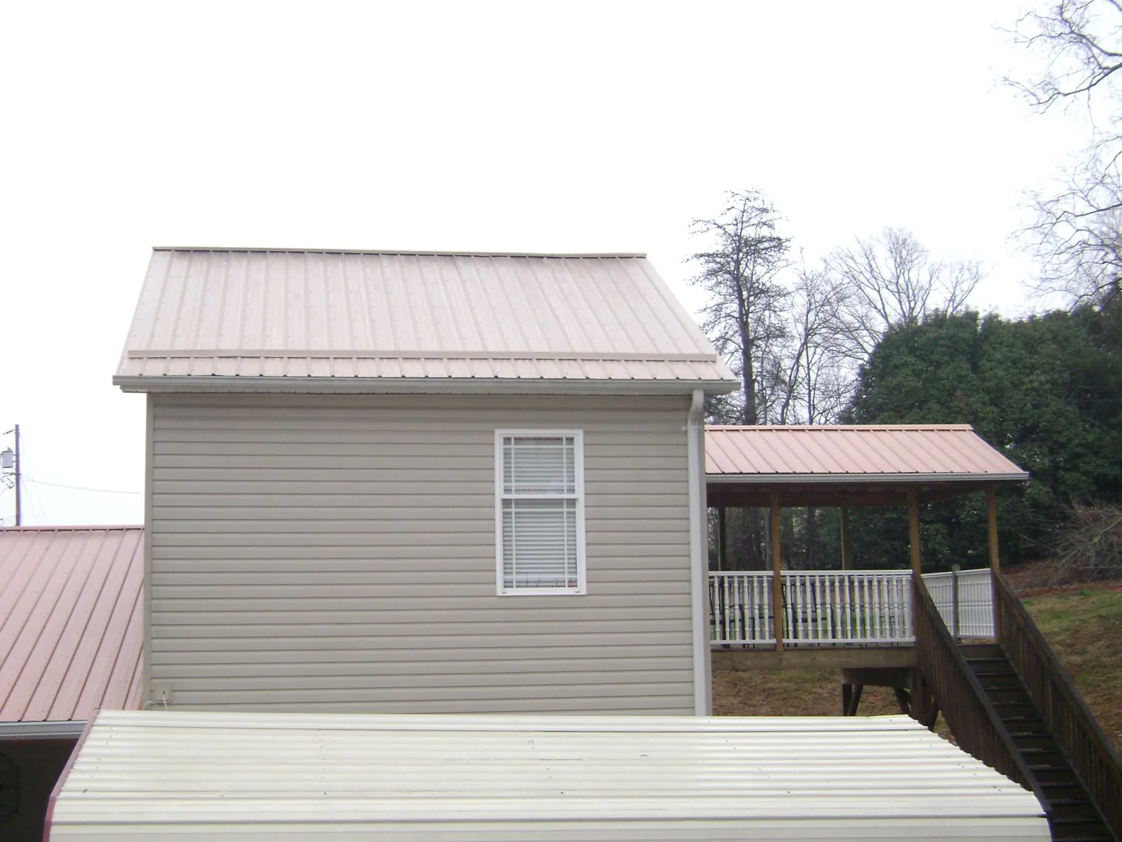Tan metal roofs on a two story addition and attached porch, from a Roof Replacement job in Hinckley